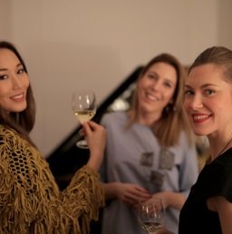 A photo of three beautiful foreign women smiling while each holding a glass of white wine
