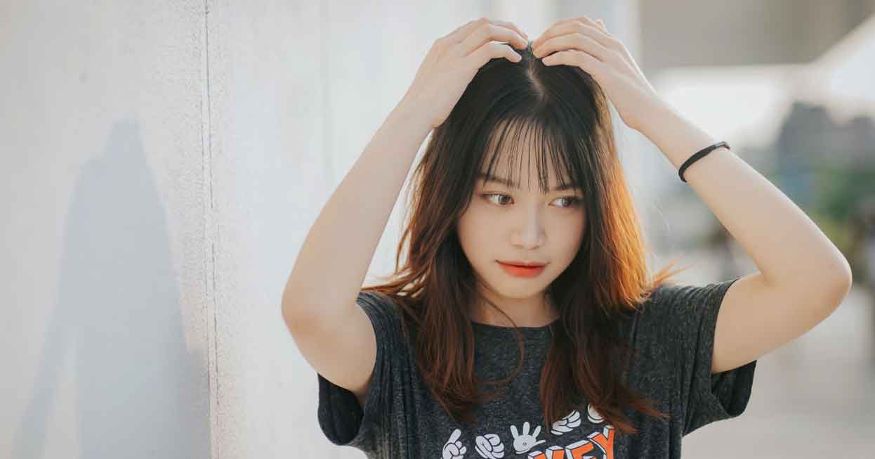 girl touching her hair next to a wall