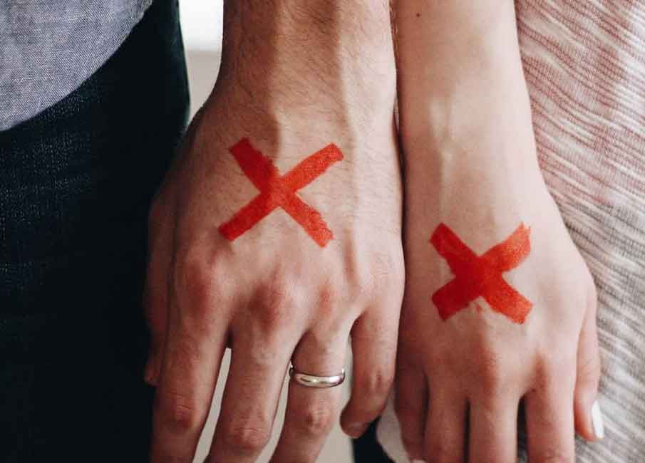 A photo of a man’s and a woman’s hands with red Xs on them.